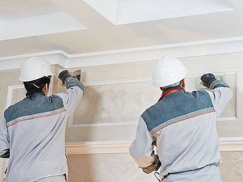 Zwei Arbeiter mit Helmen verspachteln eine Wand
