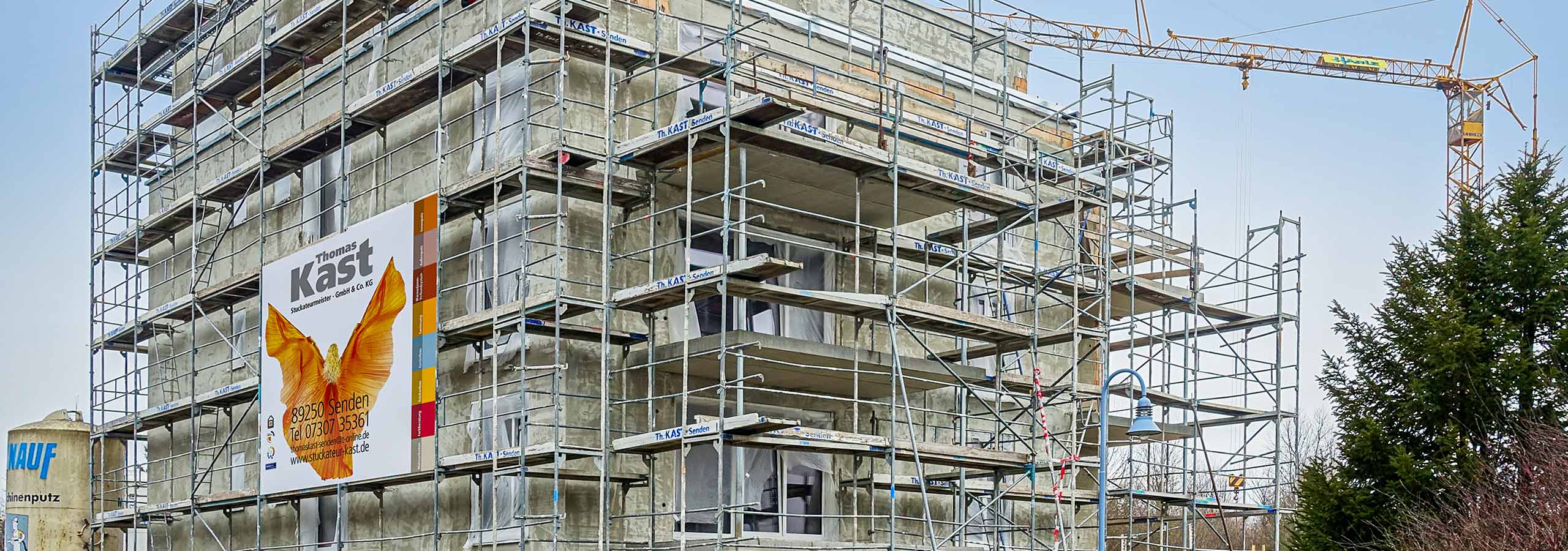 Komplett eingerüsteter Rohbau eines Mehrfamilienhauses mit einem großen Werbebanner der Kast GmbH & Co. KG am Baugerüst.